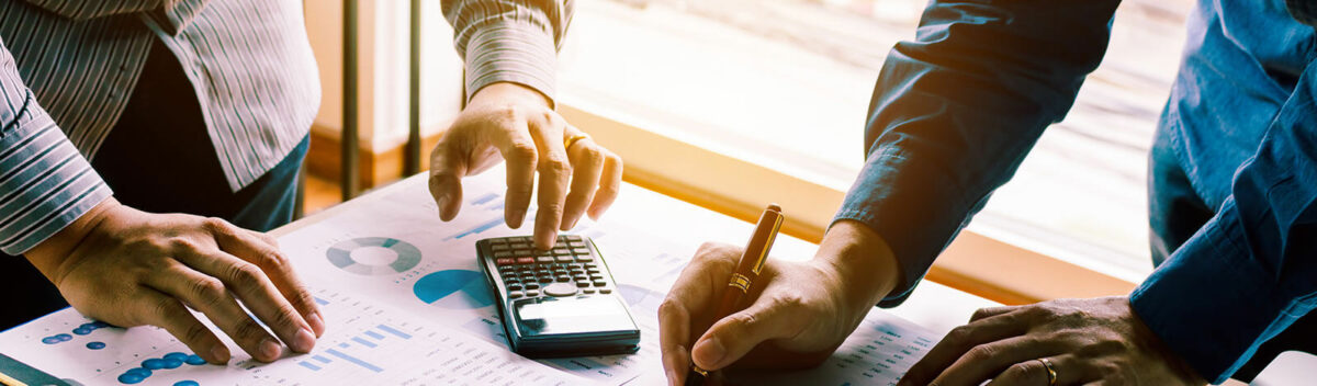 Group of business professionals at a table writing and calculating with papers scattered.