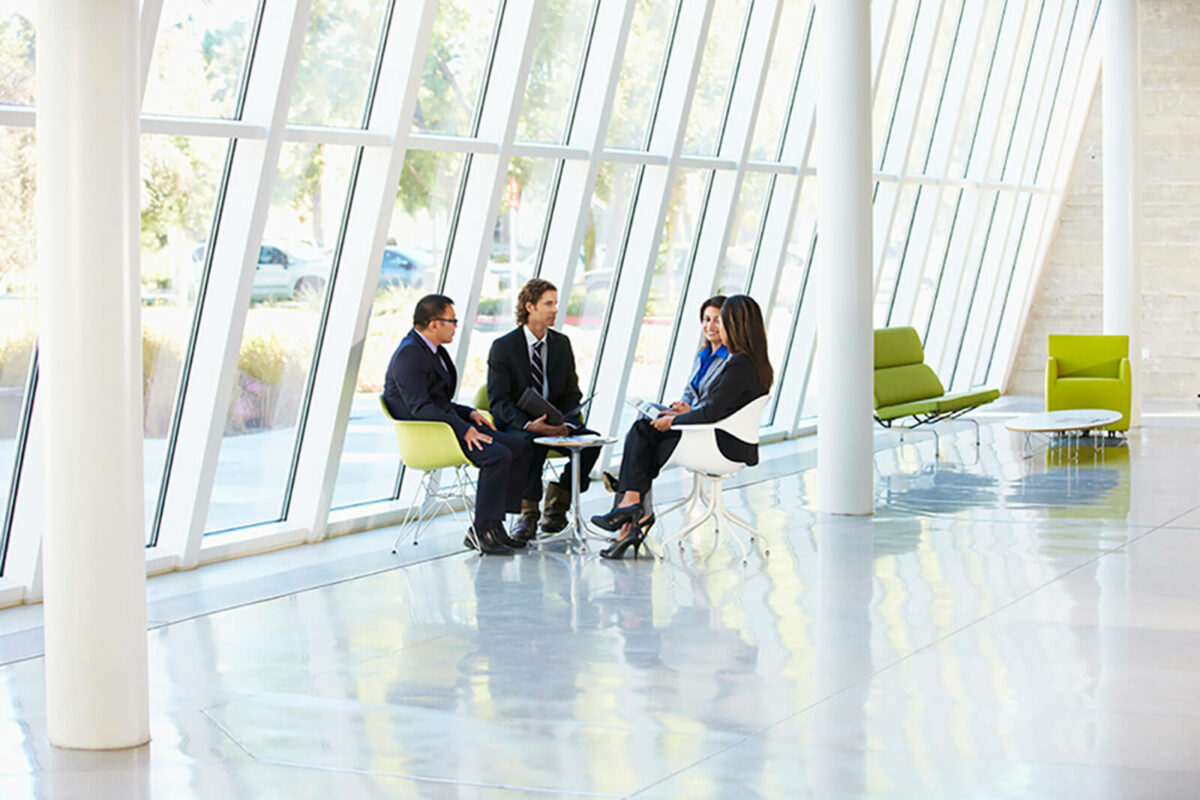 Three business professionals sitting and talking at a table in a room full of windows