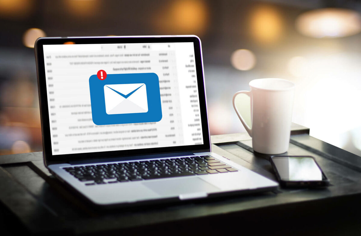 Computer, phone, and coffee cup on a desk. The computer screen is showing an email alert.