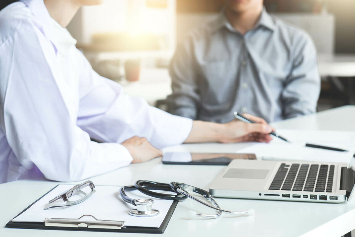 Two people sitting at a table going over papers in front of them. A stethoscope is beside the person lying on a clipboard.