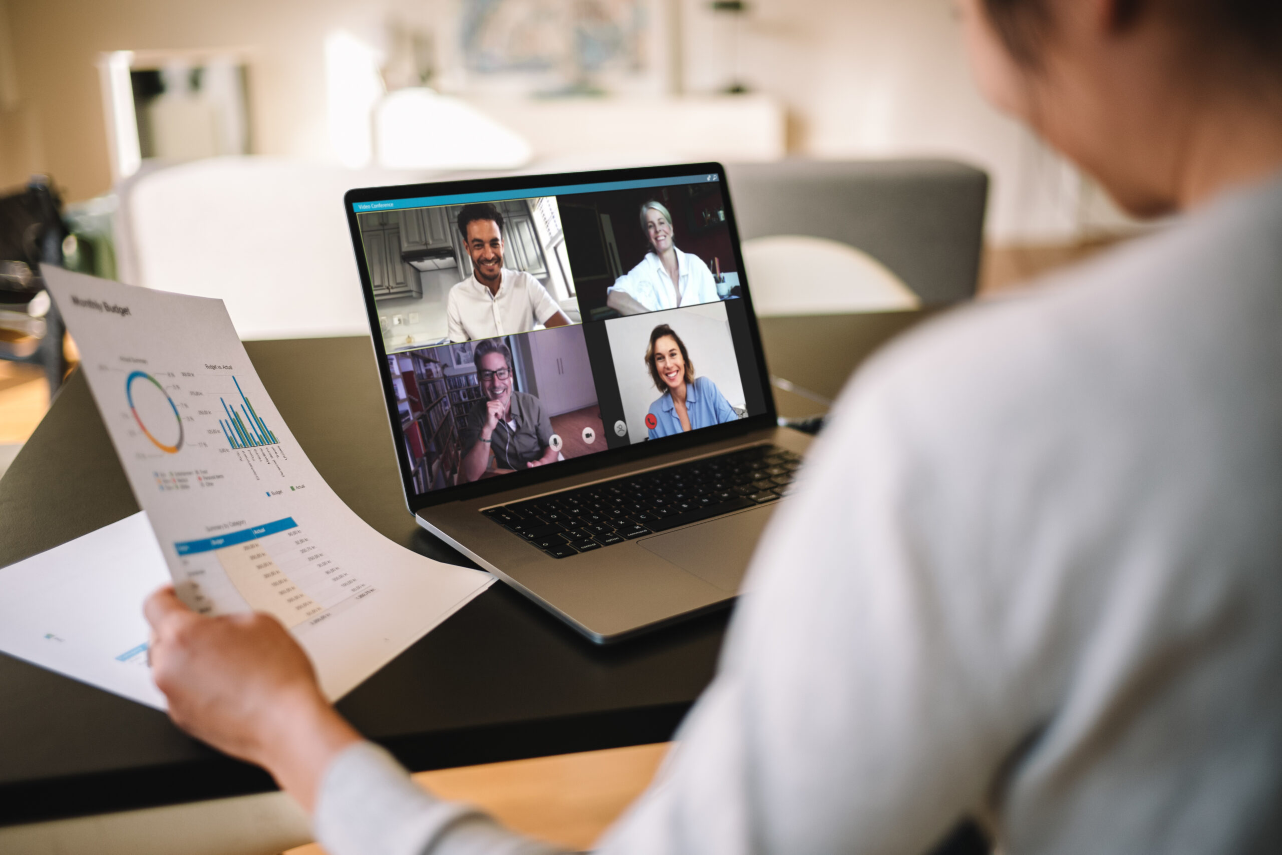 Woman sitting at desk on her laptop in a virtual meeting discussing paperwork.