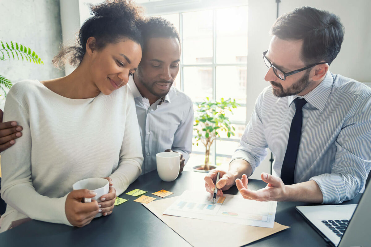 A couple sitting with a business professional discussing the papers in front of them.