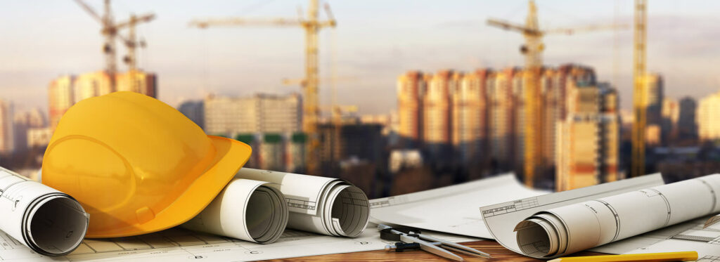A construction hat and plans sit in the foreground, while the image of an industrial factory hangs in the foreground.