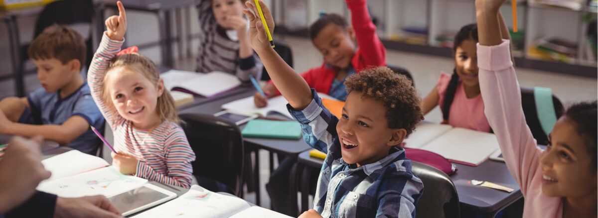 A group of students smile eagerly while raising their hands.